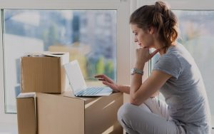 Woman looking at a laptop on top of boxes organizing her moving day